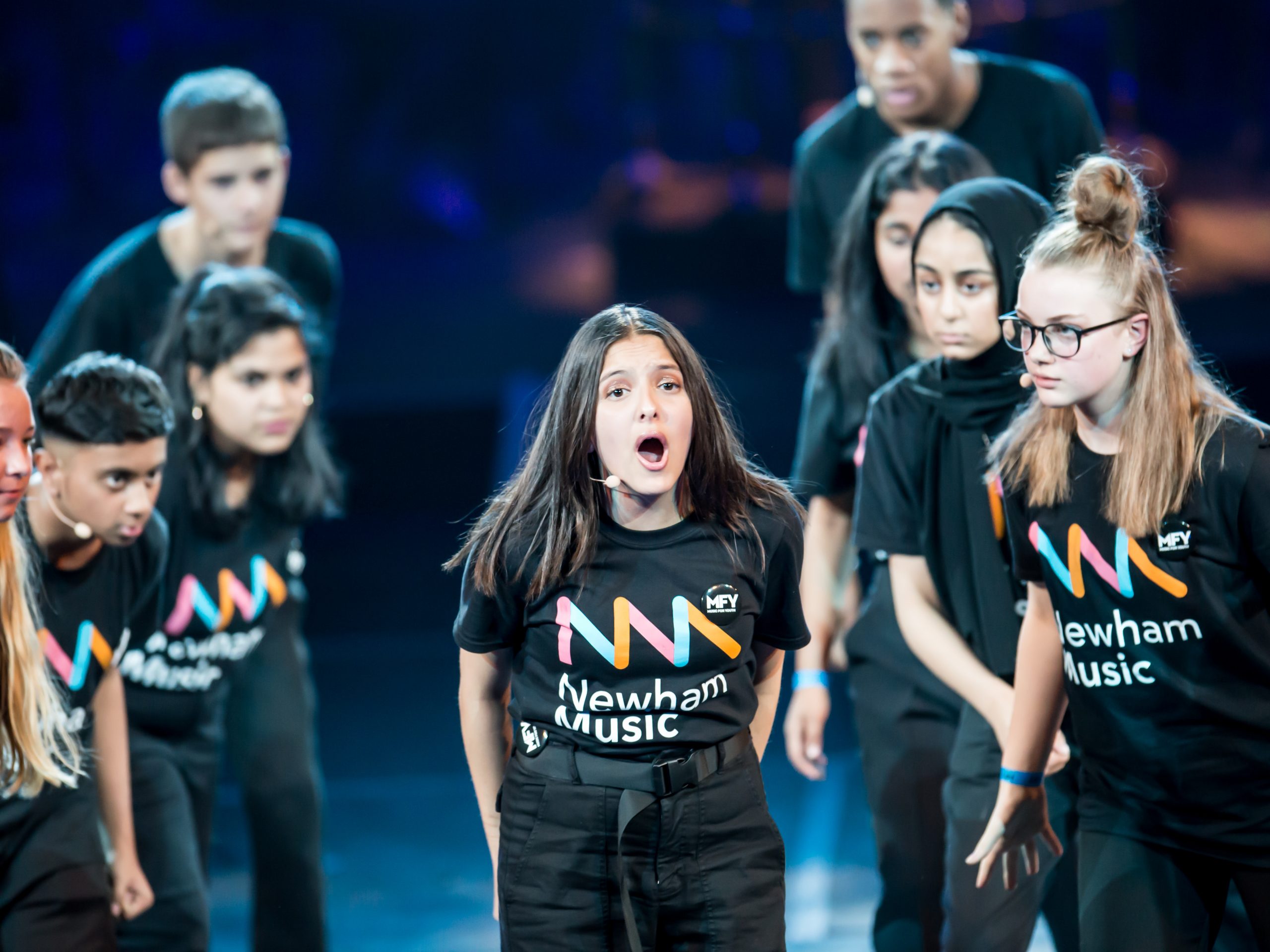 A group of young people on stage, wearing Newham Music tshirts