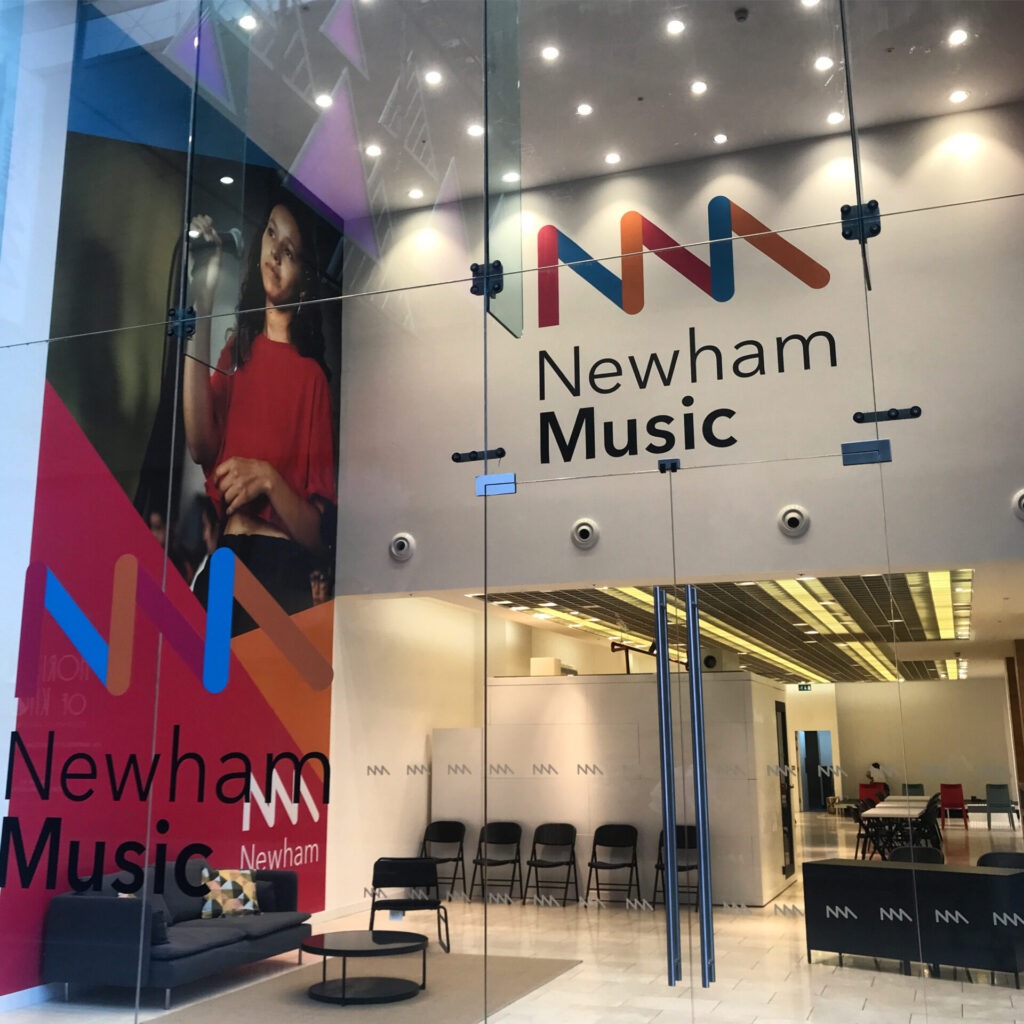 A glass fronted shop with Newham Music branding and large photograph of a young singer on the wall. There are chairs, sofa and welcome desk on display.